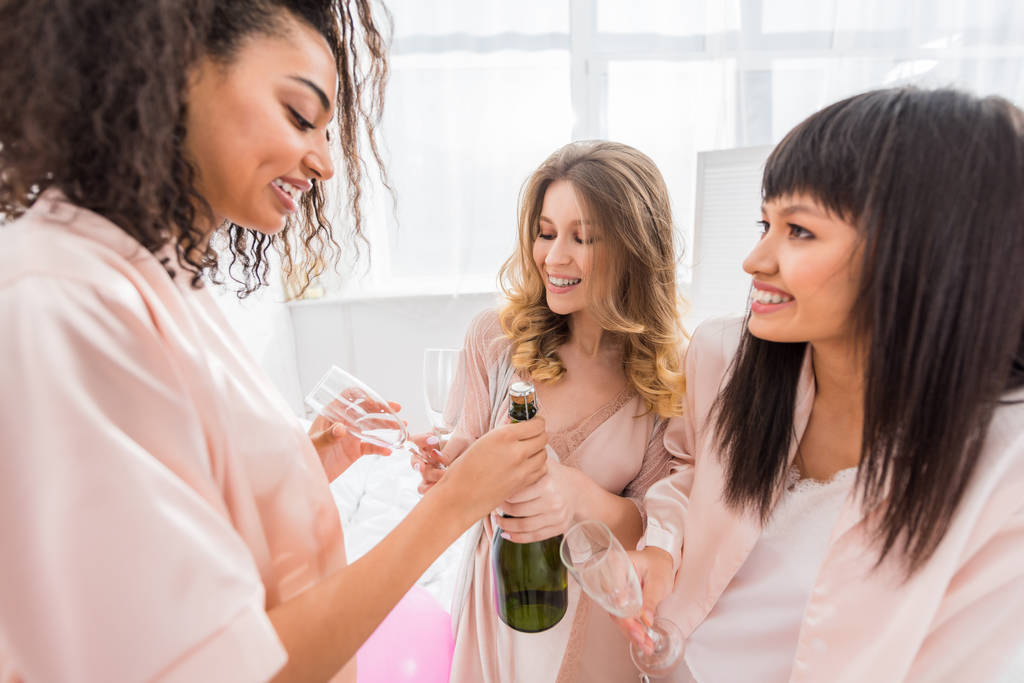 smiling multiethnic girls opening bottle of champagne on bachelorette party - Photo, Image