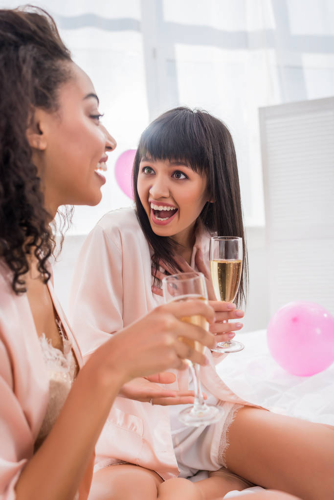 здивовані мультикультурні подружки в келихах шампанського говорять на вечірці піжами
 - Фото, зображення