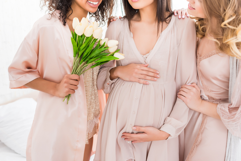 bijgesneden weergave van jonge zwangere vrouw met vriendinnen en tulp bloemen op baby shower  - Foto, afbeelding