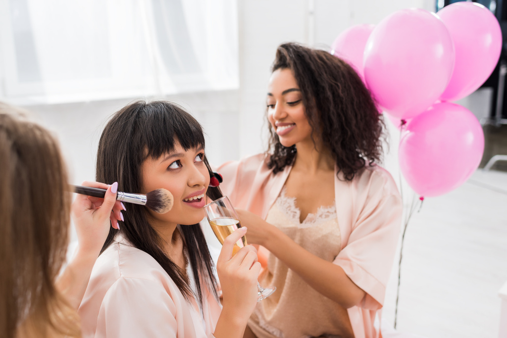 chicas multiétnicas haciendo peinado, maquillaje y beber champán en despedida de soltera
 - Foto, imagen
