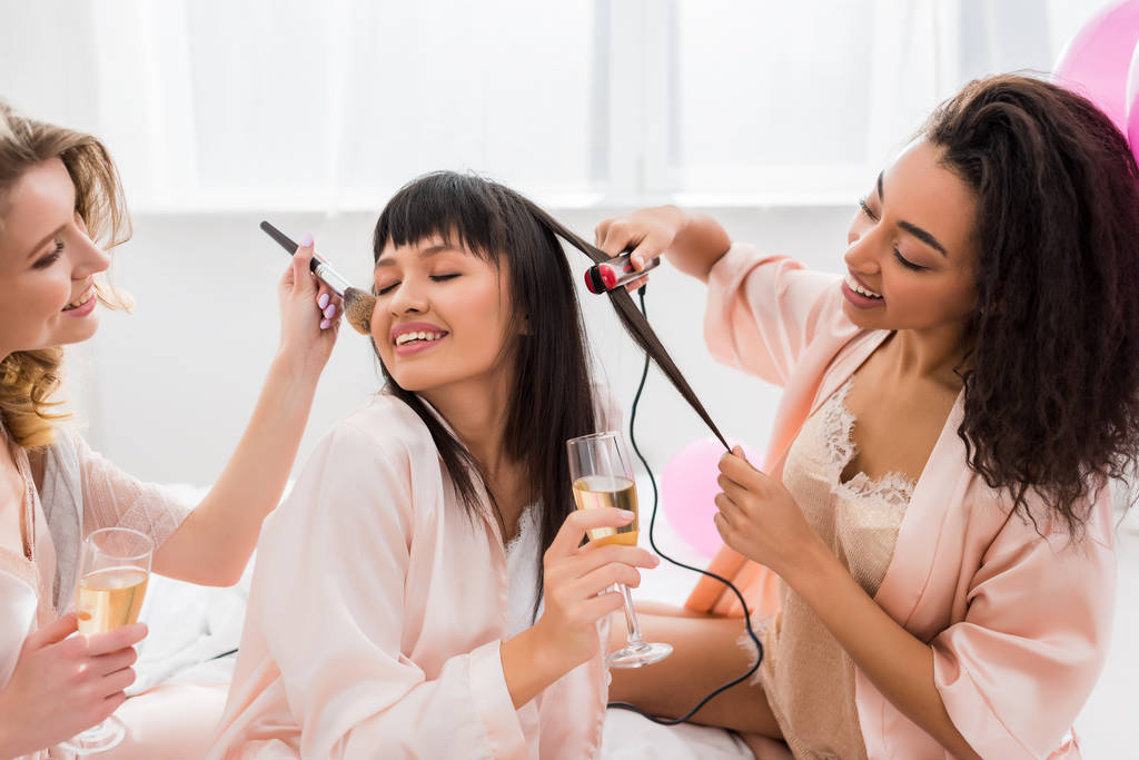 happy multiethnic girlfriends making hair styling, makeup and drinking champagne on bachelorette party - Photo, Image