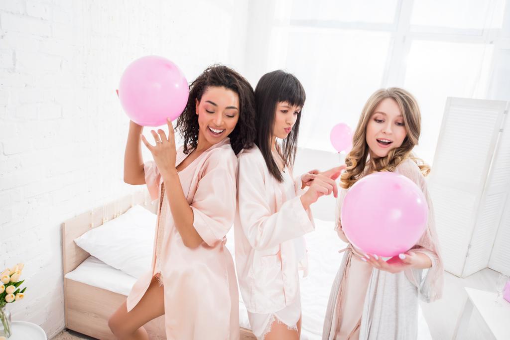 sonrientes chicas multiculturales bailando con globos rosados en despedida de soltera
 - Foto, imagen