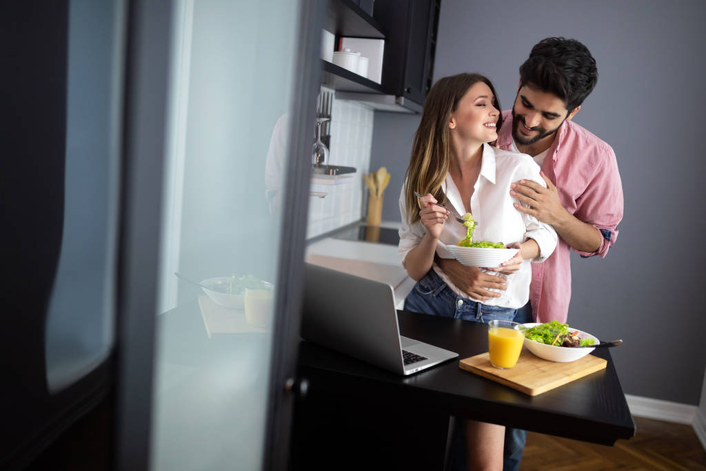 Bella giovane coppia giocosa mangiare insalata insieme in cucina - Foto, immagini