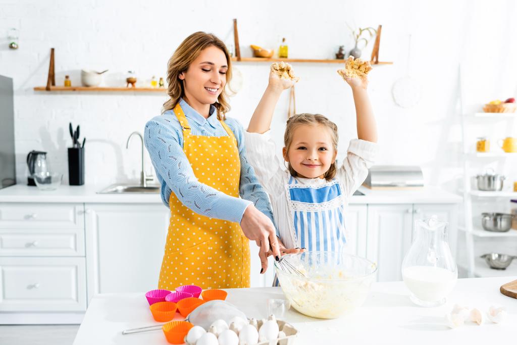 sorrindo mãe e filha em aventais misturando massa na cozinha
  - Foto, Imagem