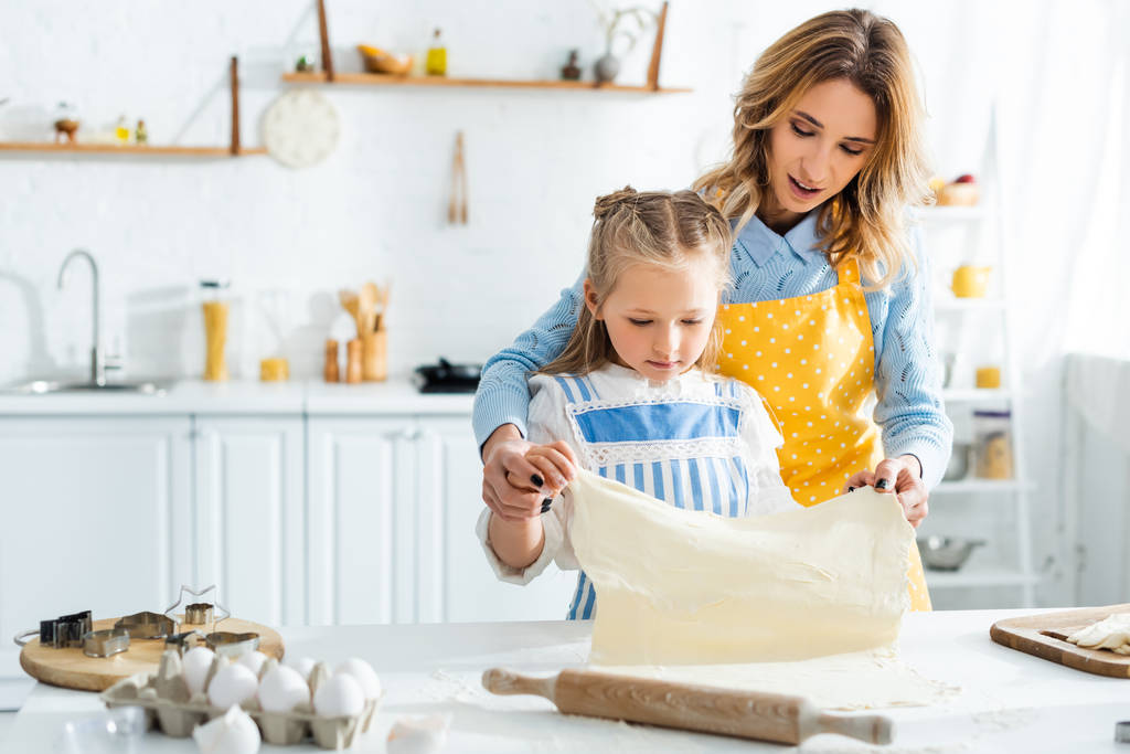 mère attrayante et fille mignonne tenant la pâte pendant la cuisson dans la cuisine
  - Photo, image