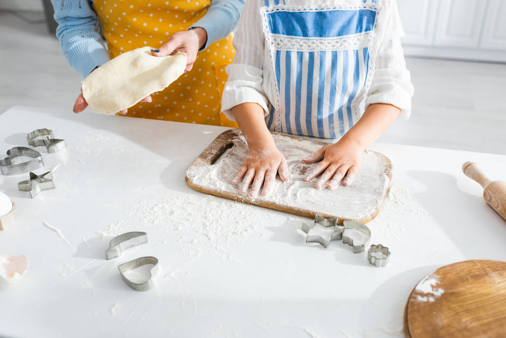 vue recadrée de la mère tenant la pâte et sa fille ajoutant de la farine dans la cuisine
  - Photo, image