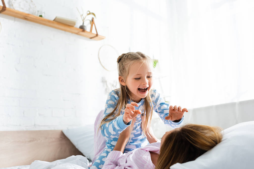 мать держит и играет с улыбающейся дочерью на кровати
   - Фото, изображение