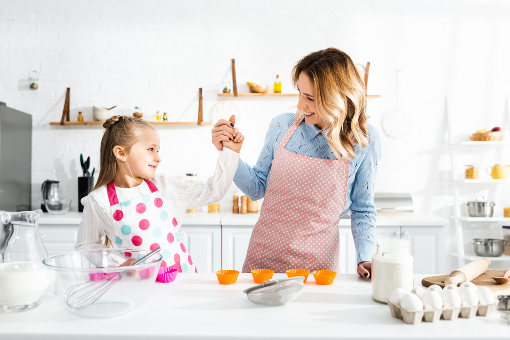 usmívající se matka drží za ruce s roztomilou dcerou v kuchyni  - Fotografie, Obrázek