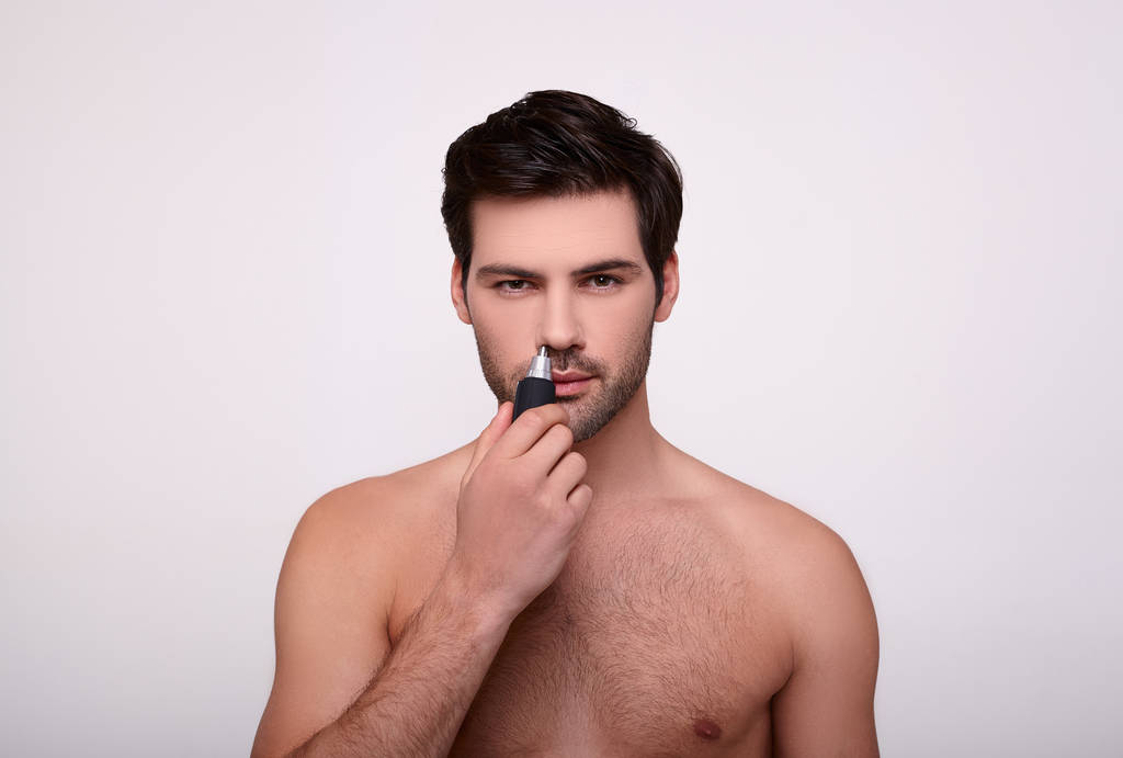 Όμορφος γενειοφόρος άντρας με μουστάκι χρησιμοποιεί κόφτη δύναμης για να κουρέψει τα μαλλιά στη μύτη.. - Φωτογραφία, εικόνα