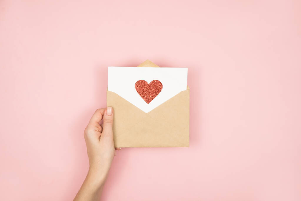 Liefdesbrief in vrouwenhanden op Valentijnsdag. Handgemaakte ansichtkaart met rood hart op roze achtergrond. 14 februari concept - Foto, afbeelding