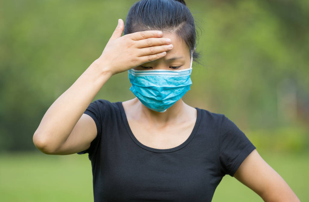 Aasialainen nainen musta t-paita kasvoissa naamio koskettaa päätä ulkona
 - Valokuva, kuva