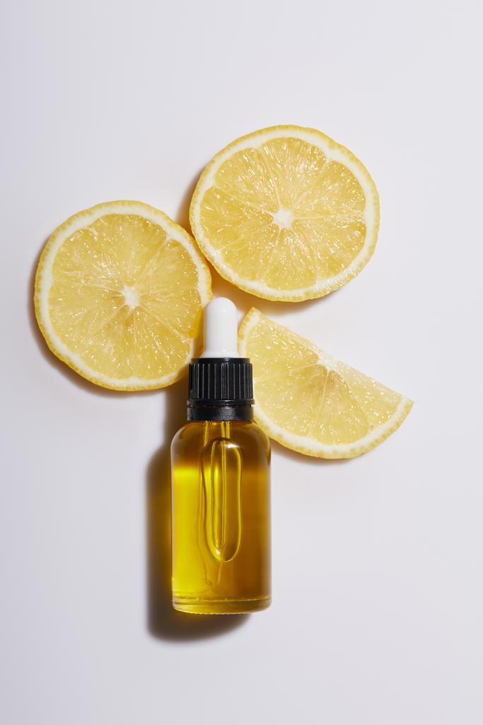 Vista superior da garrafa de óleo cosmético com fatias de limão no fundo branco
 - Foto, Imagem