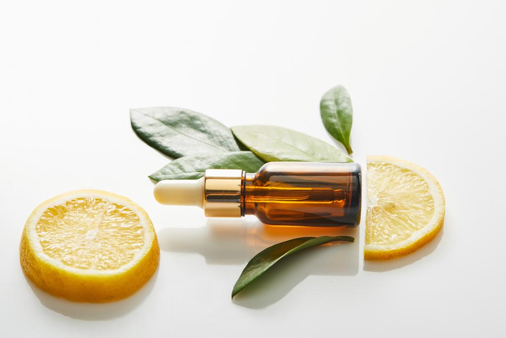 Top view of bottle of cosmetic oil with leaves and slices of lemon around on white background, panoramic shot  - Photo, Image