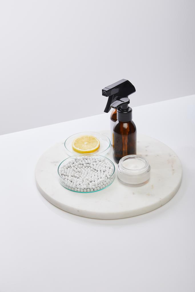 Высокий угол обзора бутылок с маслом, косметическим кремом и лабораторной стеклянной посудой с лимоном и бусами, изолированными на сером
 - Фото, изображение