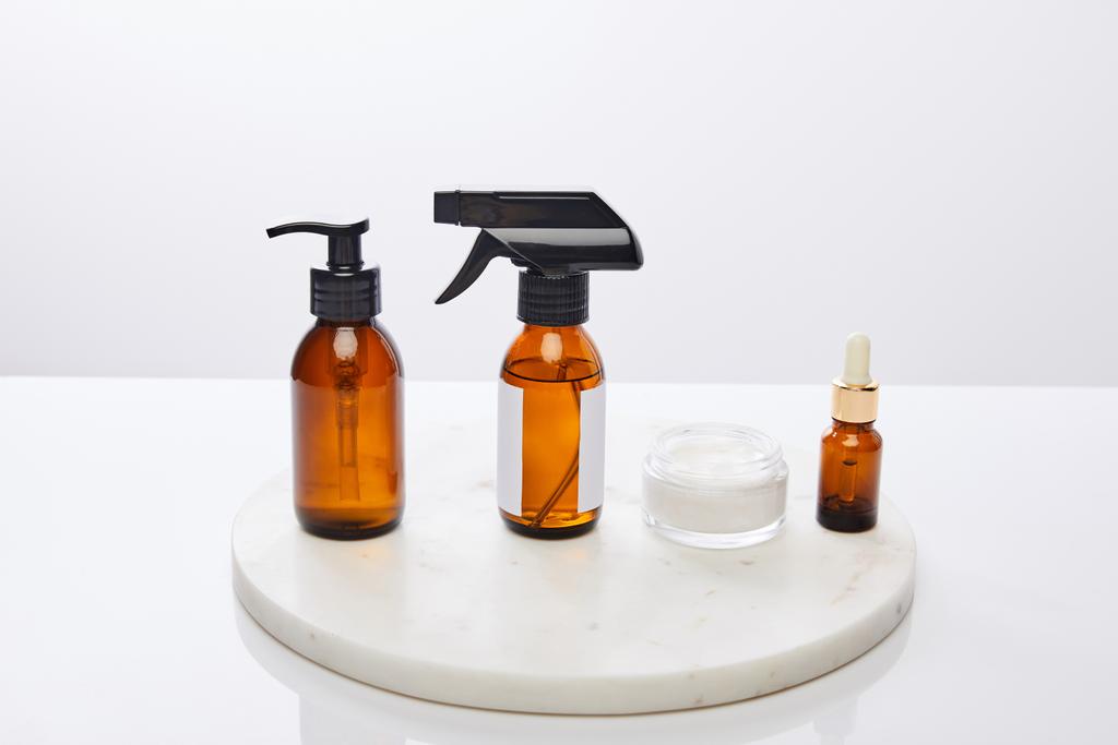 Dávkovač lahví oleje a kosmetické krém na kulatém stojanu izolované na šedé  - Fotografie, Obrázek