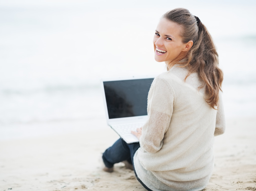 vrouw in trui zittend op het strand met laptop - Foto, afbeelding