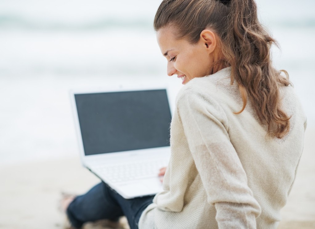 vrouw in trui zittend op het strand met laptop - Foto, afbeelding