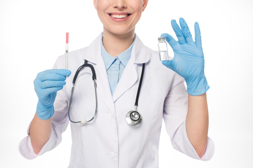 白い上に隔離されたワクチンで注射器と瓶を保持笑顔医師の作物ビュー - 写真・画像