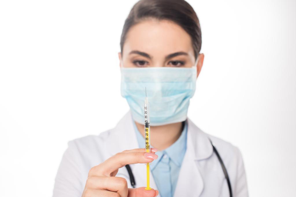 Selektywne skupienie uwagi lekarza w masce medycznej trzymającej strzykawkę na białym - Zdjęcie, obraz