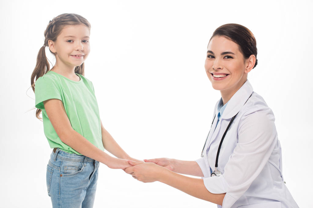 Улыбающийся педиатр и ребенок, держась за руки и улыбаясь в камеру, изолированную на белом
 - Фото, изображение