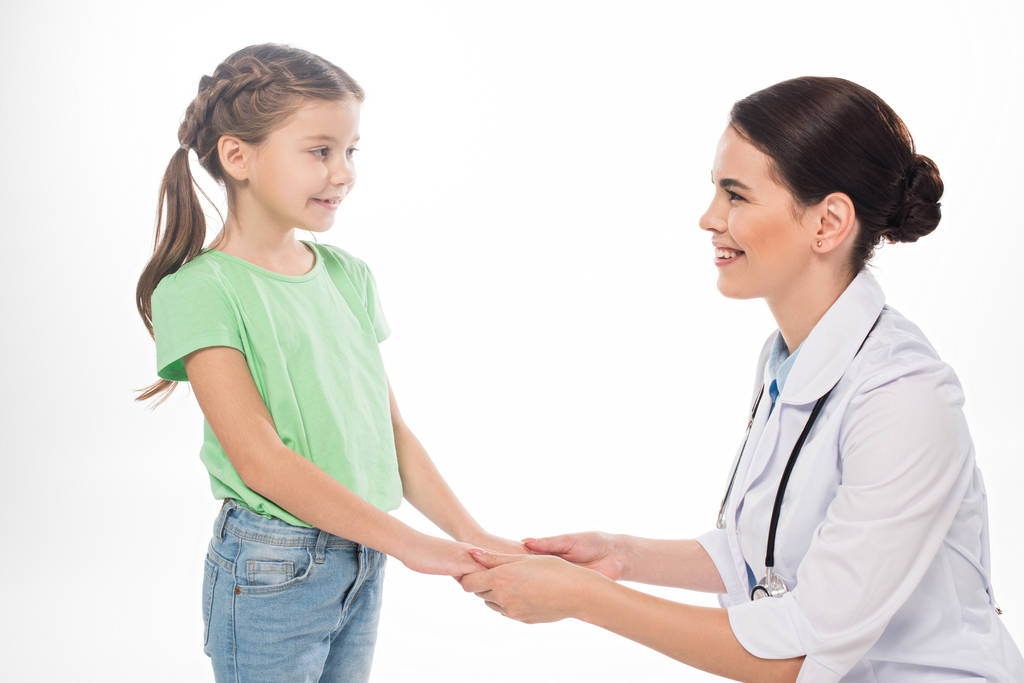 Боковой вид педиатра и малыша, держащихся за руки и улыбающихся друг другу на белом фоне
 - Фото, изображение