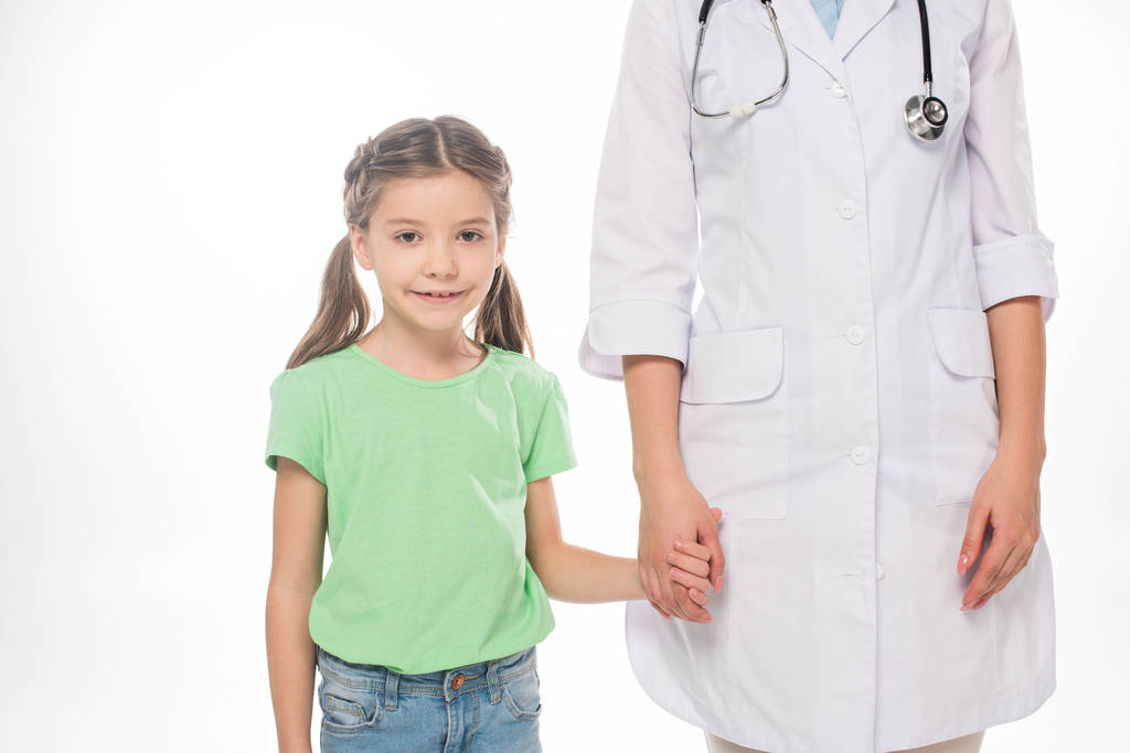 Hymyilevä lapsi katselee kameraa pitäen kädessään valkoisella eristettyä lastenlääkäriä
 - Valokuva, kuva