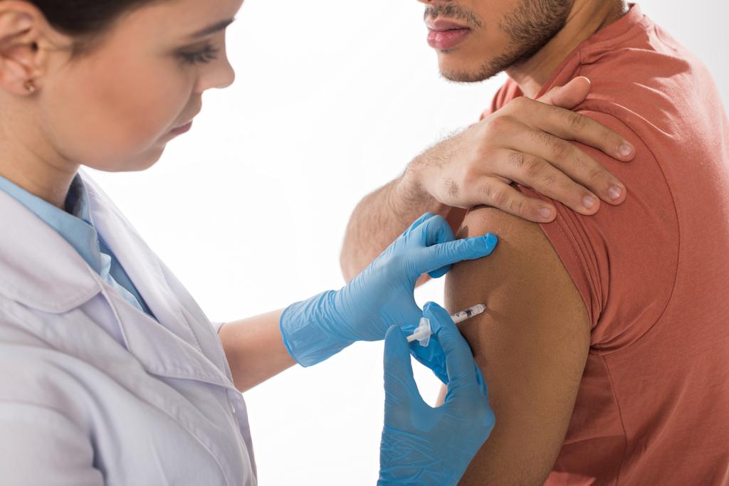Селективный фокус врача, делающего инъекцию вакцины в плечо больного, изолированного на белом
 - Фото, изображение