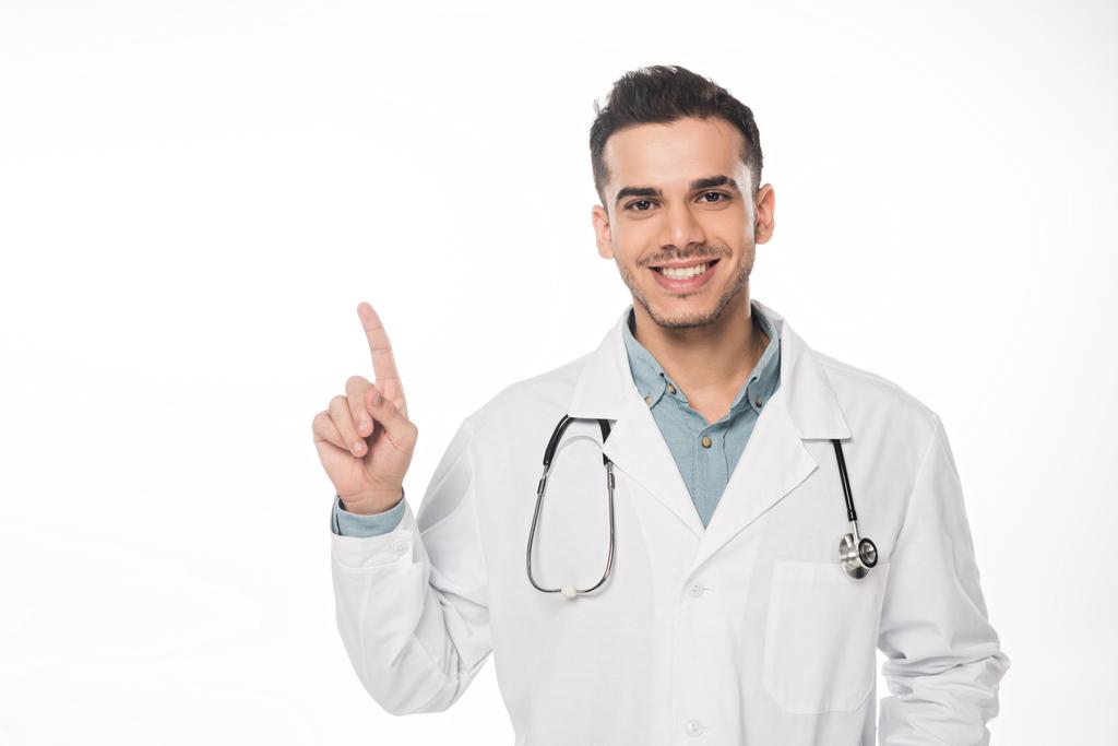 Guapo médico señalando con el dedo y sonriendo a la cámara aislada en blanco
 - Foto, Imagen