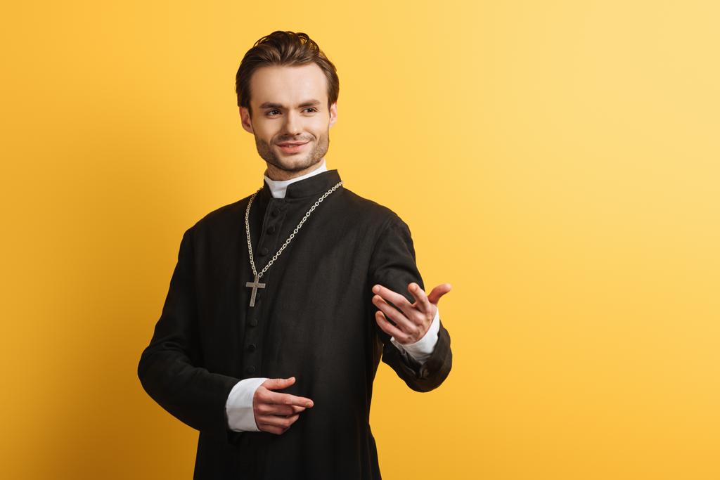 黄色で隔絶された顔をしながら手を伸ばして立つカトリックの司祭の笑顔 - 写真・画像