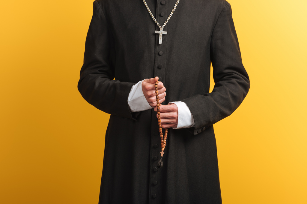 vista recortada del sacerdote católico sosteniendo cuentas de rosario de madera aisladas en amarillo
 - Foto, imagen