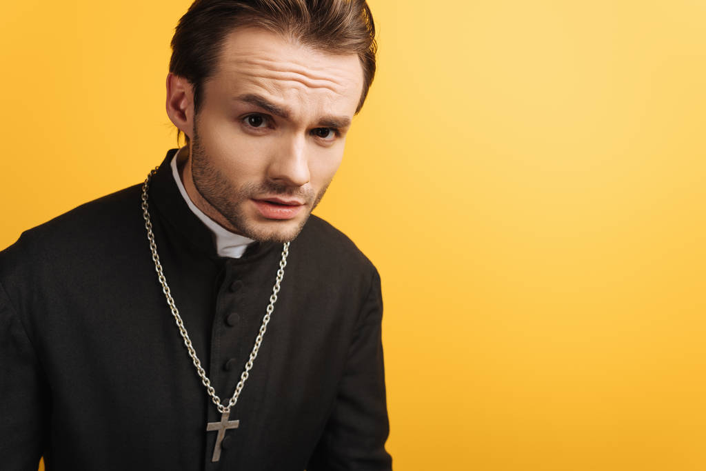 jovem padre católico pensativo olhando para câmera isolada no amarelo
 - Foto, Imagem