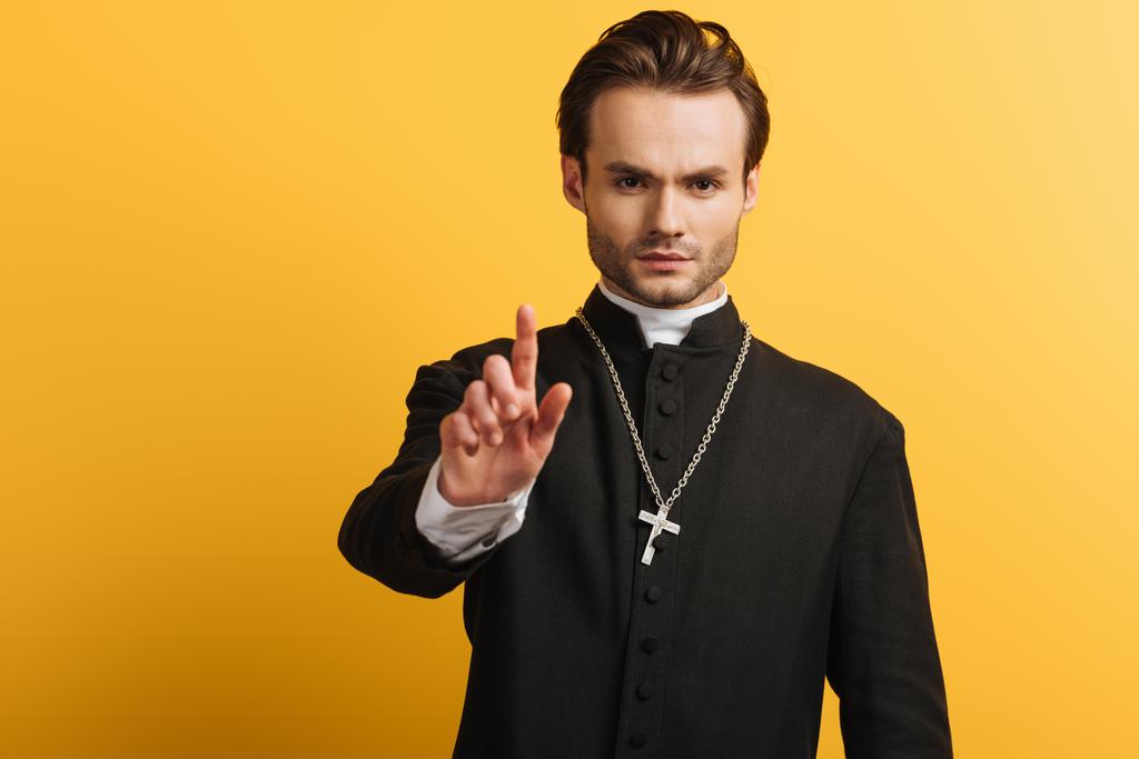 serious catholic priest showing warning gesture isolated on yellow - 写真・画像