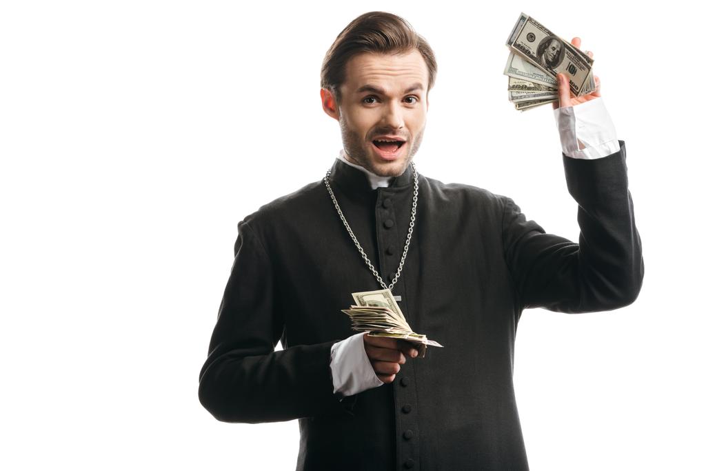 prêtre catholique excité regardant la caméra tout en montrant des billets en dollars isolés sur blanc
 - Photo, image