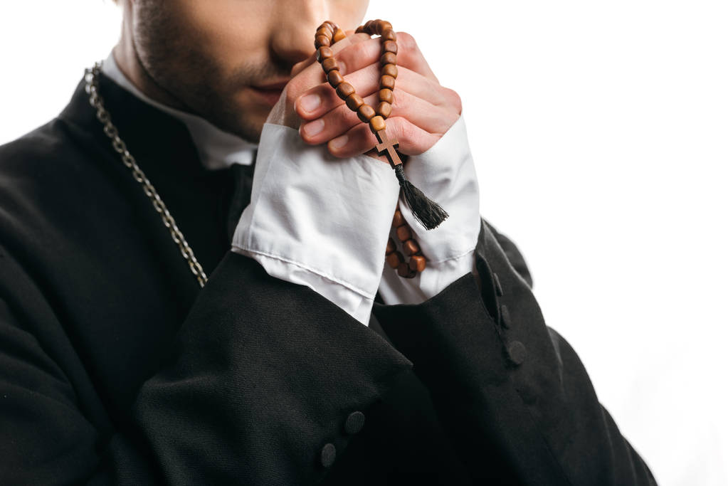 gedeeltelijk uitzicht op katholieke priester bidden terwijl het houden van houten rozenkrans kralen in de buurt gezicht geïsoleerd op wit - Foto, afbeelding