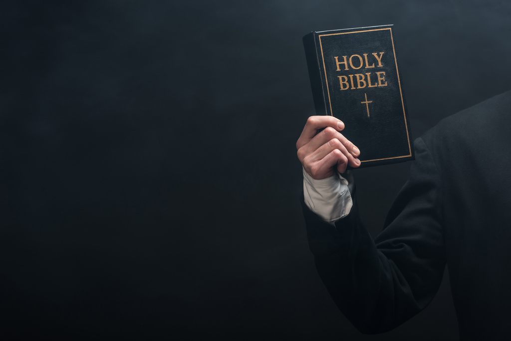 καλλιεργημένη άποψη καθολικού ιερέα που κρατά την Αγία Γραφή απομονωμένη στα μαύρα - Φωτογραφία, εικόνα