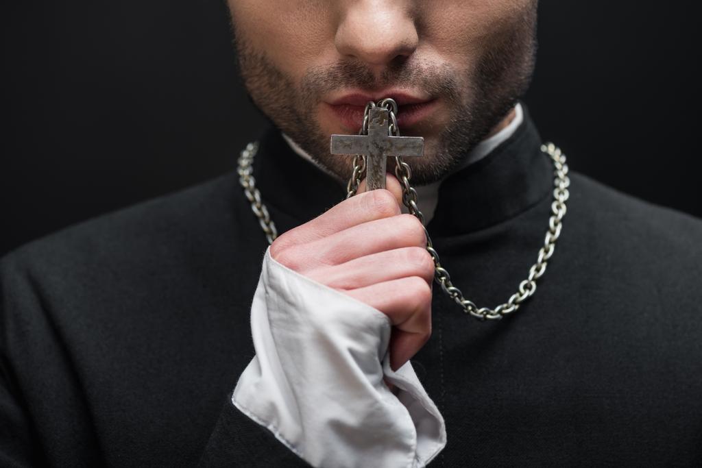 abgeschnittene Ansicht des katholischen Priesters küsst silbernes Kreuz auf seiner Halskette isoliert auf schwarz - Foto, Bild