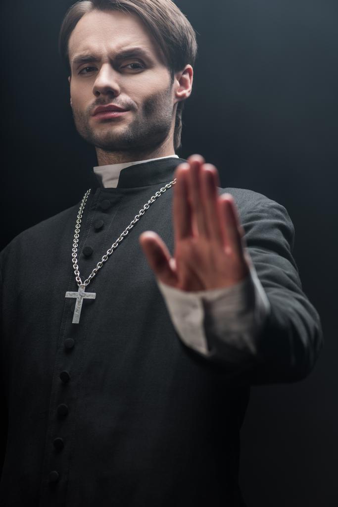 vista basso angolo di rigoroso prete cattolico mostrando rifiuto gesto isolato su nero
 - Foto, immagini