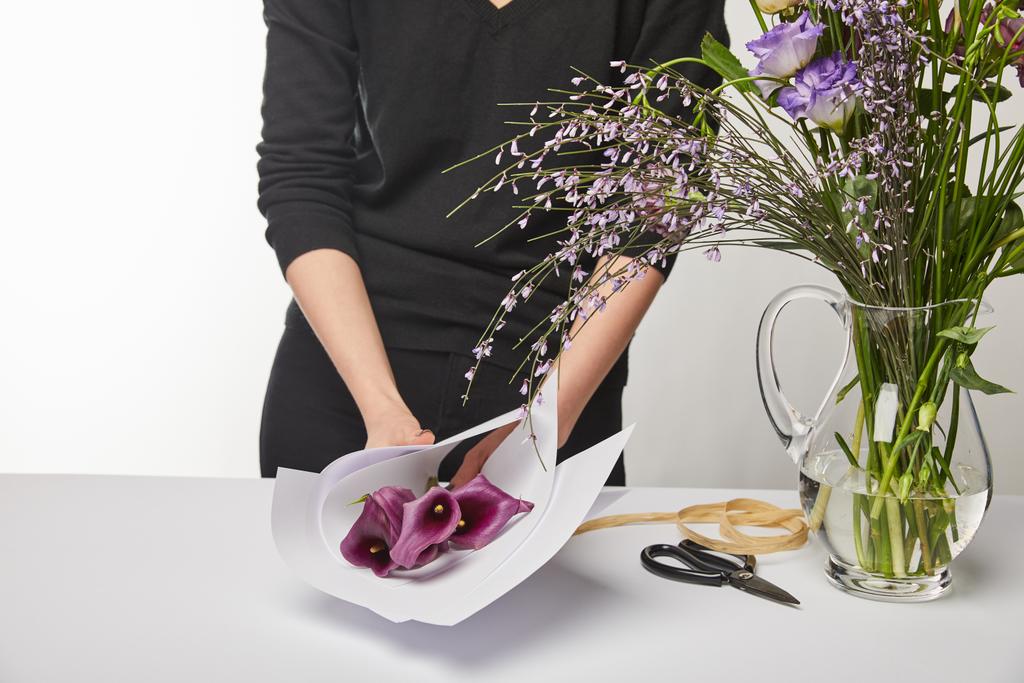 vista recortada de floristería envolviendo flores de cala púrpura en papel aislado en blanco
 - Foto, Imagen