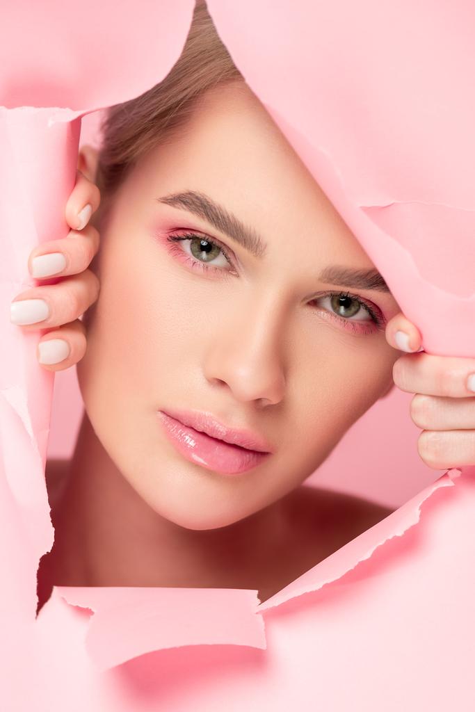 krásná žena s růžovým make-upem v roztrhaném papíru, izolované na růžové - Fotografie, Obrázek