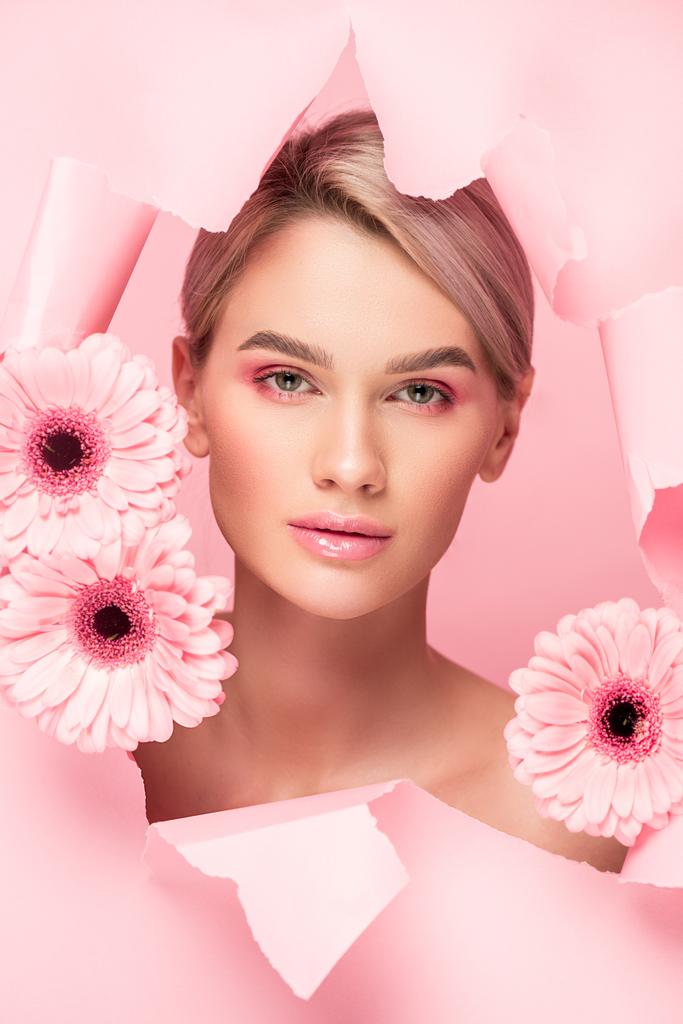 beautiful nude girl with pink flowers and makeup in torn paper, isolated on pink - Photo, Image