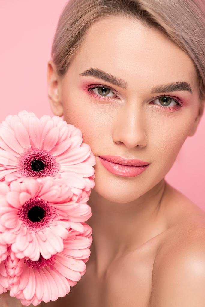 mooie jonge vrouw met roze gerbera bloemen, geïsoleerd op roze - Foto, afbeelding