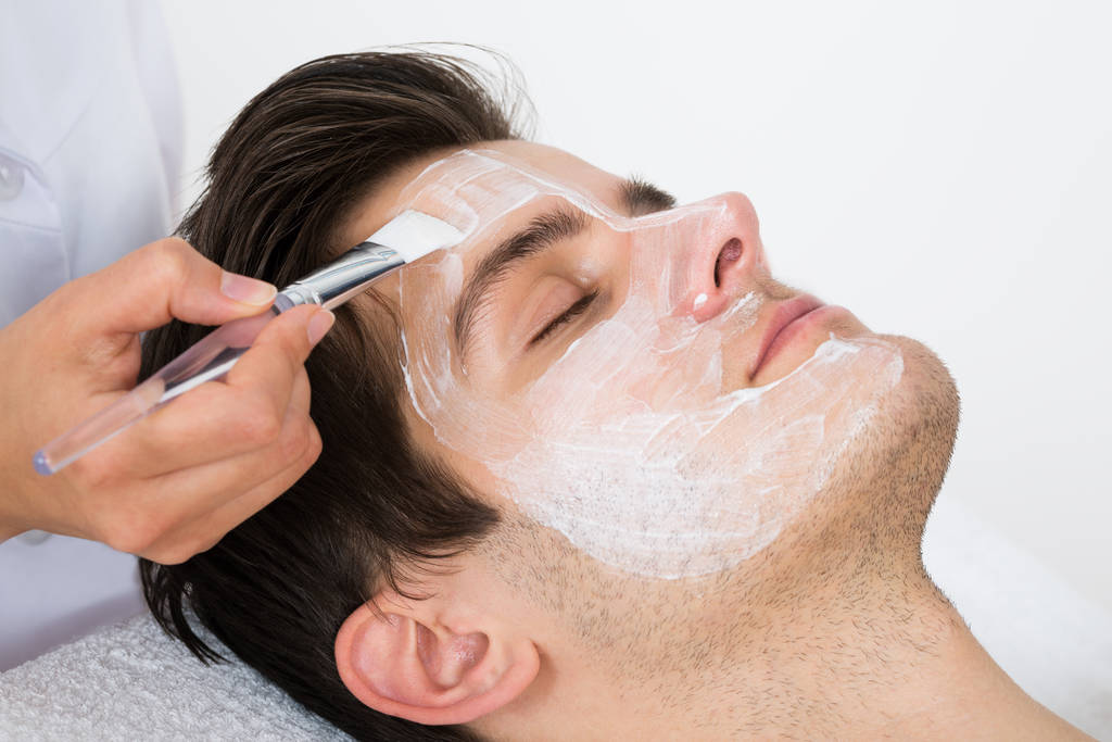 Manos de terapeuta con cepillo Aplicando mascarilla facial a un hombre joven en un spa
 - Foto, Imagen