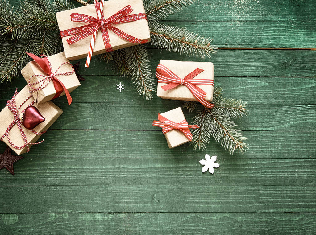 Regalos decorativos de Navidad atados con cinta roja exhibidos en ramas de pino fresco arqueadas sobre un fondo de madera verde con espacio para su saludo de Navidad
 - Foto, Imagen