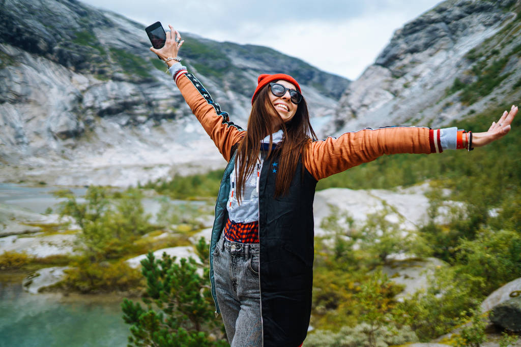 Κομψή νεαρή γυναίκα απολαμβάνει την ελευθερία της με φόντο τα βουνά της Νορβηγίας. Το κορίτσι τουρίστας απολαμβάνει το όμορφο τοπίο μεγαλοπρεπή βουνά. Ταξίδια, τρόπος ζωής, περιπέτεια, έννοια. - Φωτογραφία, εικόνα