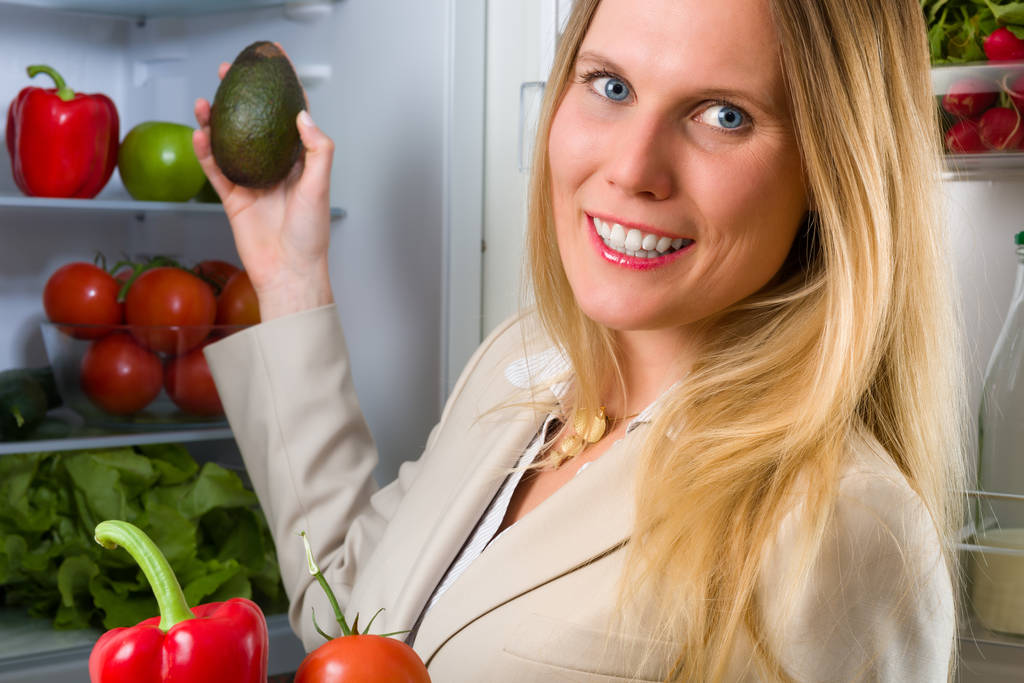 Attraente donna d'affari che mostra verdure per mangiare sano davanti a un frigorifero
 - Foto, immagini