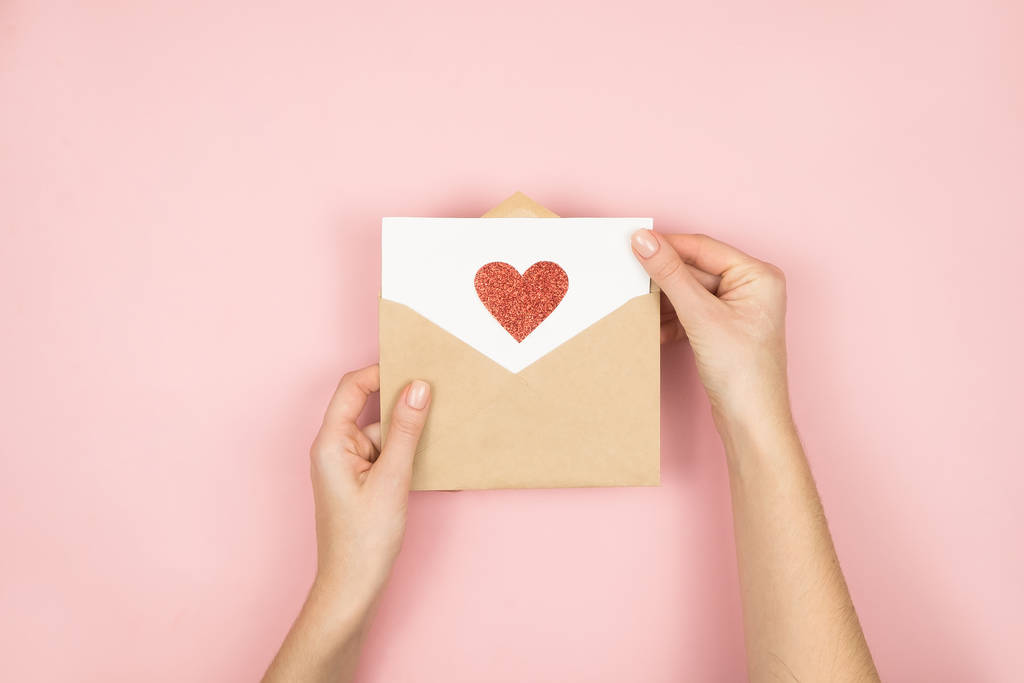 バレンタインデーに女性の手にラブレター。ピンクの背景に赤いハートの手作りポストカード。2月14日のコンセプト - 写真・画像