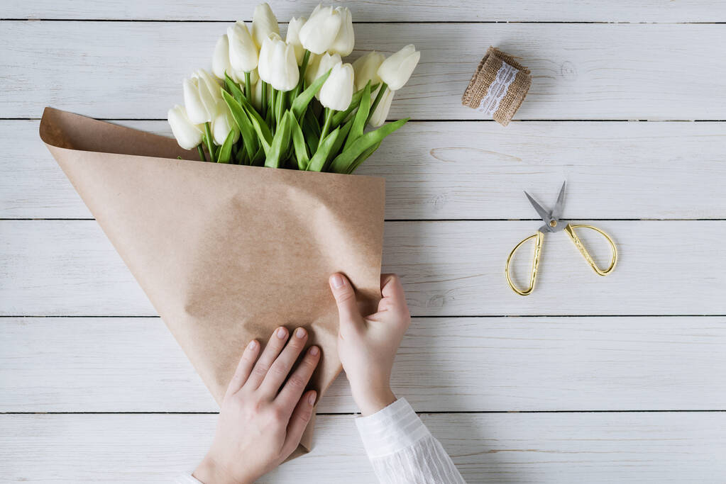 Női virágárus csomagolás gyönyörű csokor fehér tulipán csomag kézműves papír a fa asztalon. Lapos fektetés - Fotó, kép
