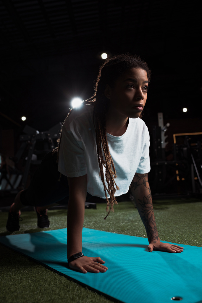 Afrikaans amerikaanse vrouw staande in plank op fitness mat in de sportschool - Foto, afbeelding