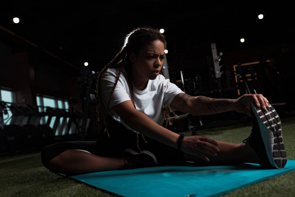 Afrikaans amerikaanse vrouw zitten en stretching op fitness mat in de sportschool - Foto, afbeelding