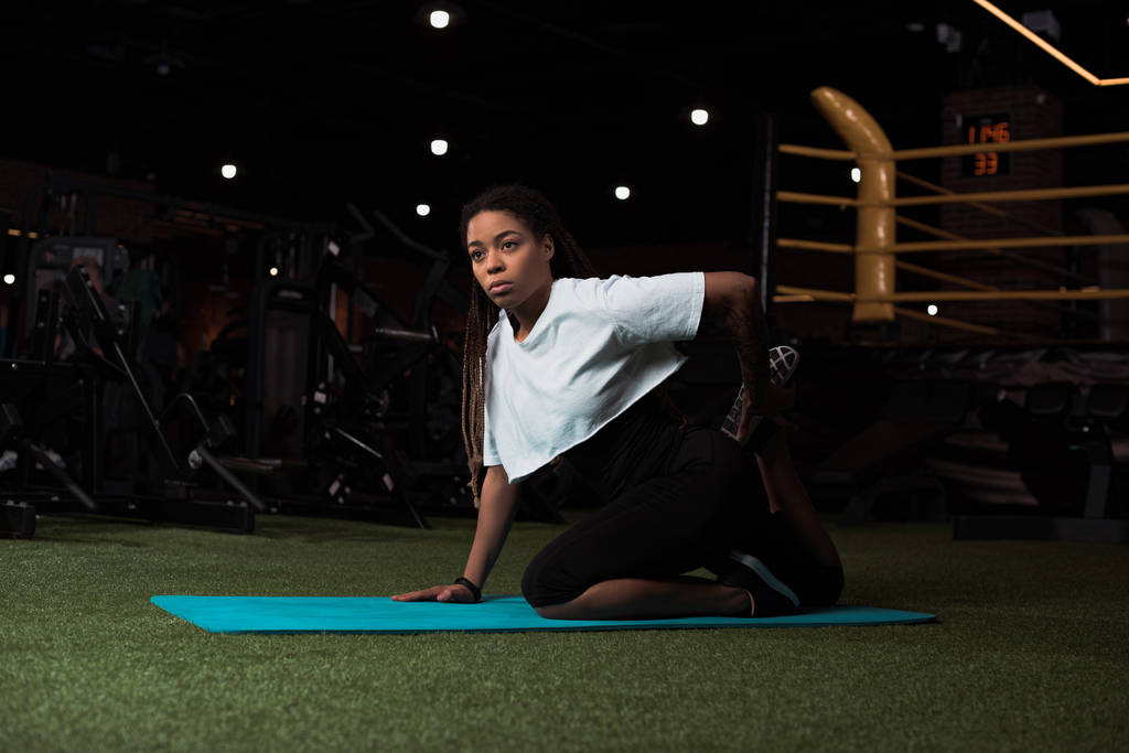 Enfoque selectivo de la mujer afroamericana sentada y estirándose en la esterilla de fitness
  - Foto, imagen